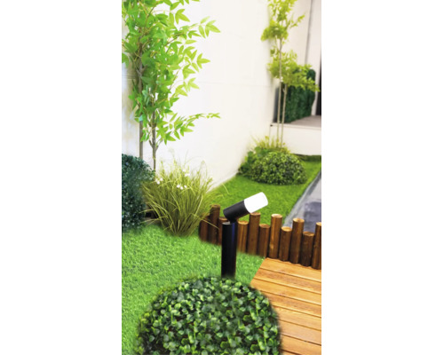 Scène de jardin moderne avec un spot extérieur LED noir, du gazon synthétique, des plantes vertes, une bordure en bois et une terrasse en bois.