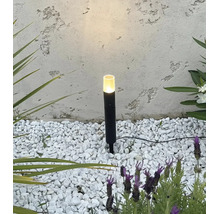 Lampe de jardin noire avec piquet dans un lit de gravier blanc devant un mur texturé.
