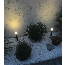 Deux spots de jardin à LED avec piquet dans un parterre de gravier et diverses plantes devant un mur crépi.