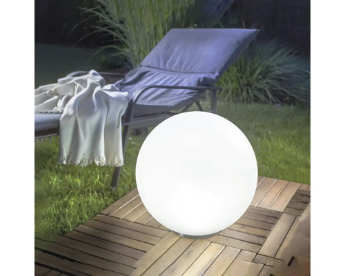 Lampe sphérique d'extérieur blanche sur une terrasse en bois dans un jardin à côté d'une chaise longue.