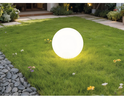 Lampe boule d'extérieur blanche lumineuse sur une pelouse verte dans un jardin.