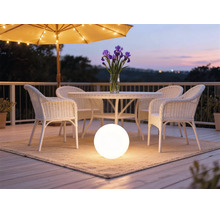 Lampe sphérique éclairée sur un tapis sous un mobilier de jardin en rotin blanc sur une terrasse organisée au crépuscule.