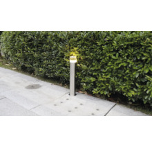 Borne lumineuse moderne en acier inoxydable dans un jardin à côté d'une haie, allumée.