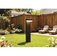 Borne lumineuse moderne sur une pelouse dans un jardin avec clôture en bois, parterres de fleurs et mobilier de terrasse.