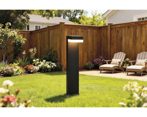 Borne lumineuse moderne sur une pelouse dans un jardin avec clôture en bois, parterres de fleurs et mobilier de terrasse.