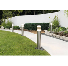 Bornes lumineuses modernes en acier inoxydable éclairant une allée de jardin claire à côté d'une pelouse et de parterres bordés de pierres.