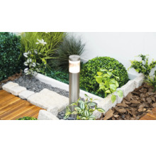 Borne lumineuse cylindrique en acier inoxydable dans un parterre de jardin moderne avec pierres et plantes.