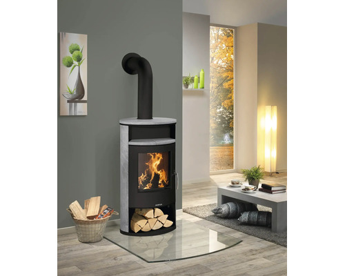 Poêle à bois Justus avec revêtement en pierre et feu de bois dans un salon de style moderne sur une plaque de sol en verre.