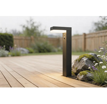 Borne d'éclairage moderne noire avec détecteur de mouvement sur une terrasse en bois à côté de pierres et de plantes dans un jardin lumineux.