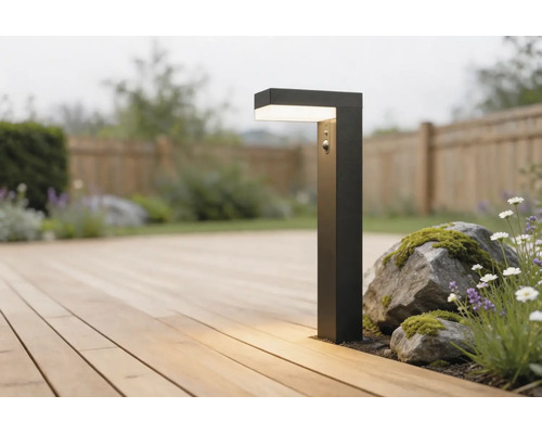 Borne d'éclairage moderne noire avec détecteur de mouvement sur une terrasse en bois à côté de pierres et de plantes dans un jardin lumineux.
