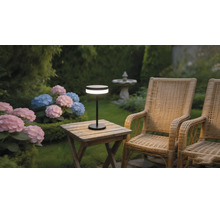Lampe de table LED portable moderne sur une table de jardin en bois à côté de fauteuils en osier et d'hortensias dans un jardin.