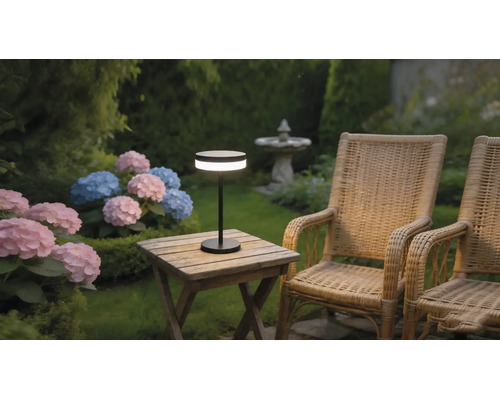 Lampe de table LED portable moderne sur une table de jardin en bois à côté de fauteuils en osier et d'hortensias dans un jardin.
