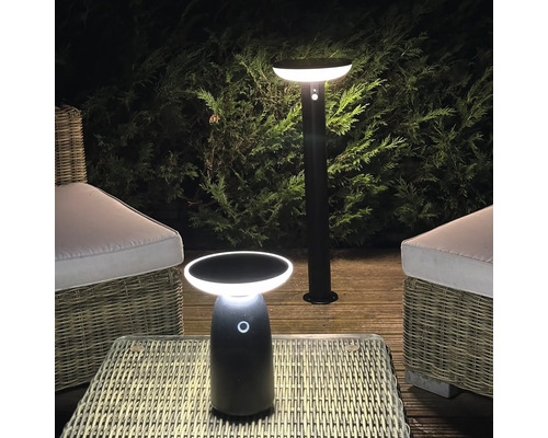 Éclairage extérieur LED moderne comprenant une borne lumineuse et une lampe de table sur une terrasse en bois avec des meubles en rotin.