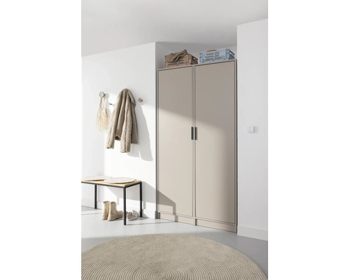 Armoire de couloir beige moderne à deux portes, avec un banc de vestiaire et un tapis rond dans une entrée lumineuse.