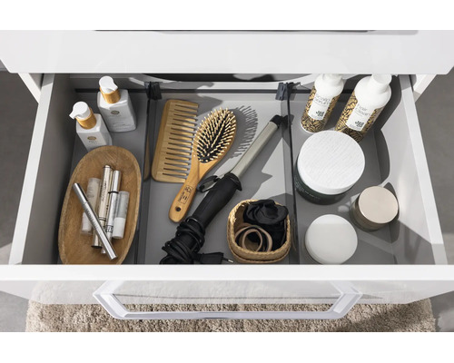 Tiroir de salle de bain ouvert et organisé avec des cosmétiques, une brosse à cheveux, un fer à boucler et des produits de soin.