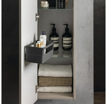 Armoire de toilette ouverte avec serviettes, flacons de cosmétiques sur des étagères en verre et une boîte de rangement sur la porte.