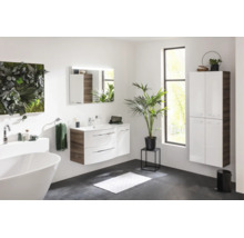 Salle de bains moderne et lumineuse avec meuble sous-vasque blanc, armoire haute suspendue, baignoire îlot et miroir éclairé.