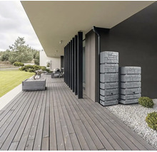 Terrasse moderne en bois avec deux récupérateurs d'eau de pluie aspect pierre contre un mur sombre, zone en gravier et bac à fleurs.