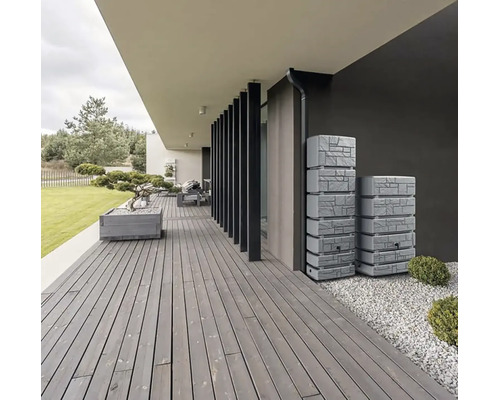 Terrasse moderne en bois avec deux récupérateurs d'eau de pluie aspect pierre contre un mur sombre, zone en gravier et bac à fleurs.