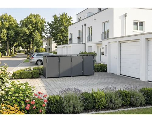 Moderne Mülltonnenbox aus Metall für vier Tonnen in einer gepflasterten Einfahrt vor einem weissen Wohnhaus mit Bepflanzung.