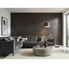 Salon moderne avec revêtement mural sombre aspect bois, canapé d'angle gris en velours, table basse ronde en béton et lampadaire arqué.