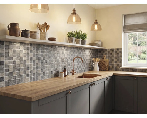 Cuisine moderne et lumineuse avec carrelage en mosaïque grise, plan de travail en bois, évier avec robinet en cuivre et suspensions en verre.