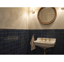 Salle de bain classique avec carrelage mural bleu foncé, lavabo en céramique blanche avec robinetterie en laiton et miroir rond.