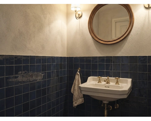 Salle de bain classique avec carrelage mural bleu foncé, lavabo en céramique blanche avec robinetterie en laiton et miroir rond.