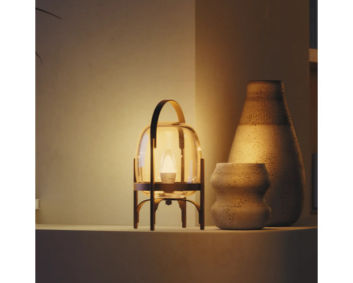 Lampe de table moderne en forme de lanterne, verre et métal, lumière chaude près de deux vases en céramique texturés sur une étagère.