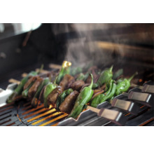 Viande et poivrons verts sur des brochettes en métal au-dessus d'une grille de barbecue chaude avec de la vapeur.