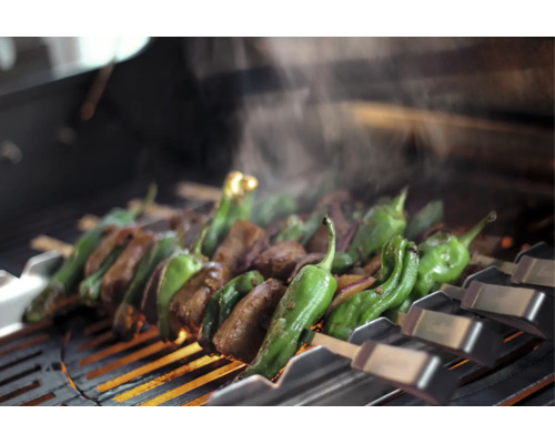 Viande et poivrons verts sur des brochettes en métal au-dessus d'une grille de barbecue chaude avec de la vapeur.