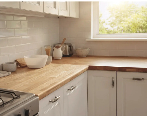 Cuisine lumineuse avec plan de travail en bois massif, meubles blancs et crédence en carreaux blancs près d une fenêtre.