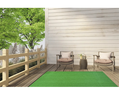 Grüner Kunstrasenteppich auf einer hellen Holzterrasse mit zwei Gartenstühlen und einem Holzzaun im Hintergrund.