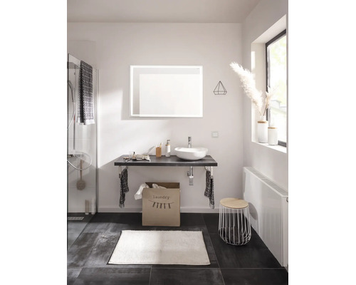 Salle de bains moderne avec vasque à poser, miroir lumineux, plan de toilette, sac à linge, radiateur et accessoires de salle de bains.