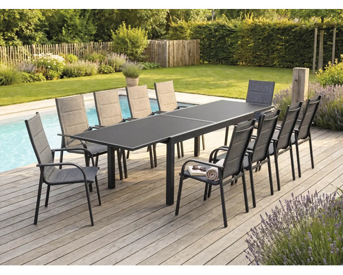 Ensemble repas de jardin avec grande table extensible gris foncé et dix fauteuils en tissu sur une terrasse en bois au bord d'une piscine.
