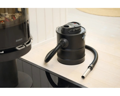 Aspirateur à cendres électrique avec réservoir en métal et tuyau d aspiration flexible dans une pièce lumineuse à côté d une cheminée.