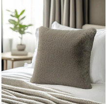 Coussin décoratif carré en fausse fourrure sur un lit avec une couverture en tricot dans une chambre lumineuse.