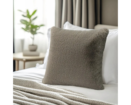 Coussin décoratif carré en fausse fourrure sur un lit avec une couverture en tricot dans une chambre lumineuse.