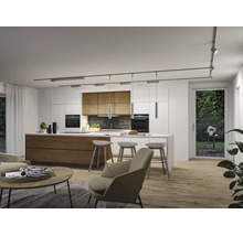 Moderne offene Küche mit Insel, Barhockern und Schienensystem an der Decke. Wohnbereich mit Sessel und Couchtisch im Vordergrund.