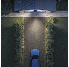 Solarbetriebene Außenleuchte über einem Garagentor beleuchtet eine Einfahrt mit einem Auto in der Draufsicht.