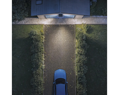 Solarbetriebene Außenleuchte über einem Garagentor beleuchtet eine Einfahrt mit einem Auto in der Draufsicht.