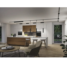 Moderne offene Küche mit Kochinsel und Schienensystem an der Decke. Helle, organisierte Atmosphäre mit Holz- und Metallelementen.
