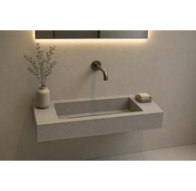 Lavabo mural rectangulaire aspect pierre avec robinetterie murale et miroir rétroéclairé dans une salle de bain moderne.