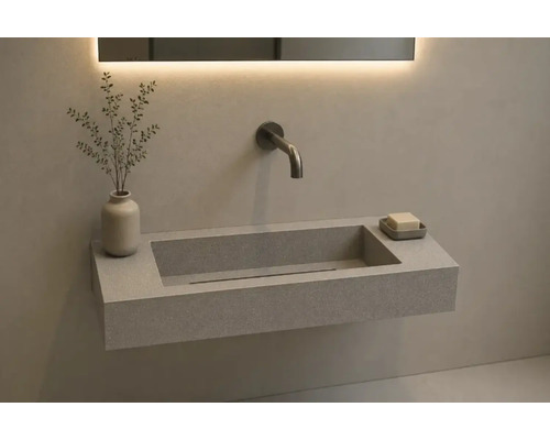 Lavabo mural rectangulaire aspect pierre avec robinetterie murale et miroir rétroéclairé dans une salle de bain moderne.