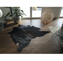 Schwarzes Kuhfell auf Holzboden in einem modernen, hellen Wohnzimmer mit Zimmerpflanze und dekorativer Kugelleuchte.