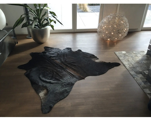 Schwarzes Kuhfell auf Holzboden in einem modernen, hellen Wohnzimmer mit Zimmerpflanze und dekorativer Kugelleuchte.
