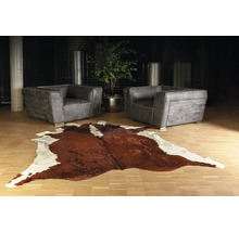 Salon moderne avec deux fauteuils en cuir gris et un tapis en peau de vache marron et blanc sur un parquet clair.