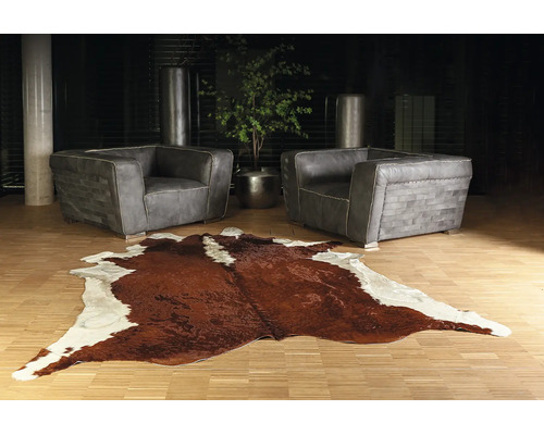 Salon moderne avec deux fauteuils en cuir gris et un tapis en peau de vache marron et blanc sur un parquet clair.