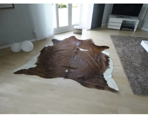 Tapis en peau de vache de forme naturelle dans un salon moderne et lumineux avec un parquet clair.