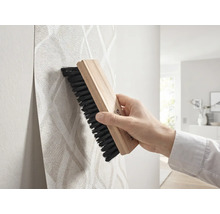 Main lissant du papier peint à motifs avec une brosse à tapisser en bois.